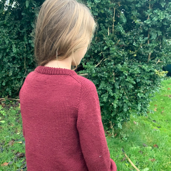 Striksweater til børn. Sandness klompelompe i farven dyb julerød, perfekt julsweater. Sweater med saddelskulder fra AlmaKnit