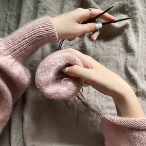 Hænder holder garnnøgle og strikkepinde. Et strikkeprojekt efter en strikkeopskrift fra almaknit, hvor du selv designer din strikkeopskrift. 